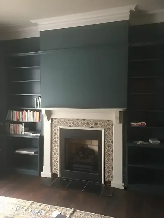 Cambridge living room in deep green with fitted bookshelves and white fireplace with tiled surround