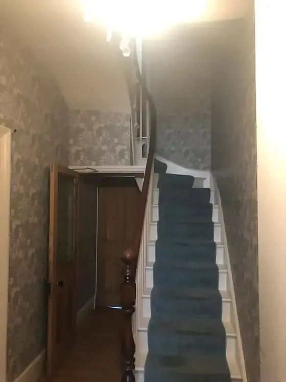 Staircase with blue-green carpet and patterned William Morris wallpaper on both walls, Cambridge hall