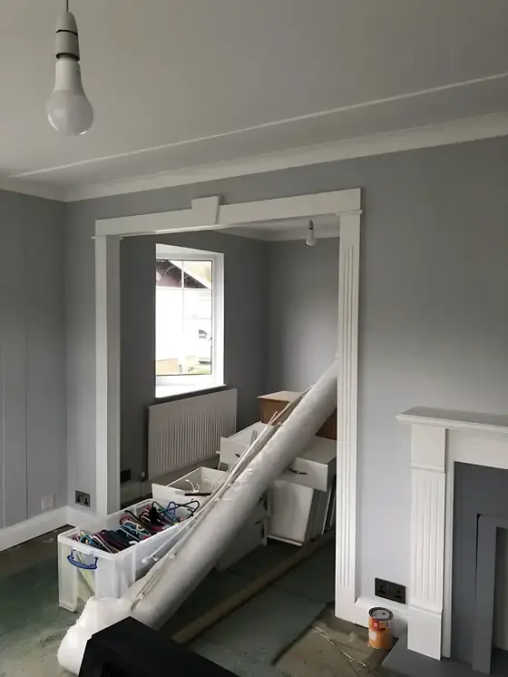 Living room redecorated in grey with white coving and doorway, with materials still on site
