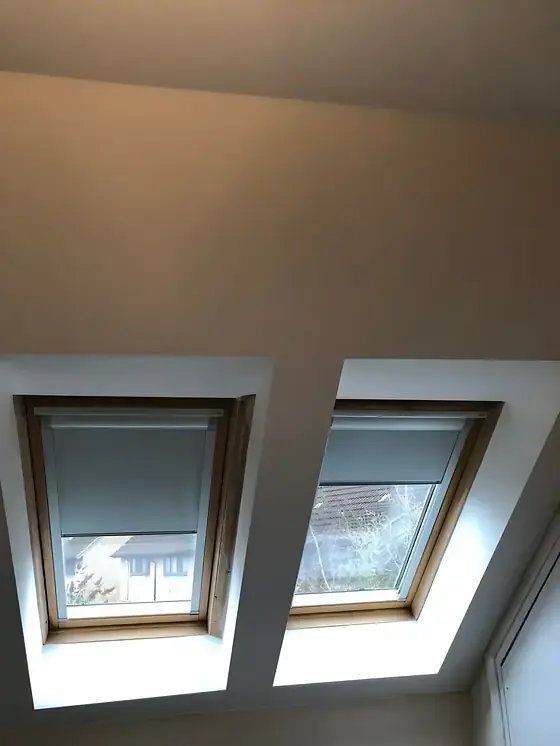 Smooth skimmed loft ceiling above twin roof windows with blinds in a Cambridge house