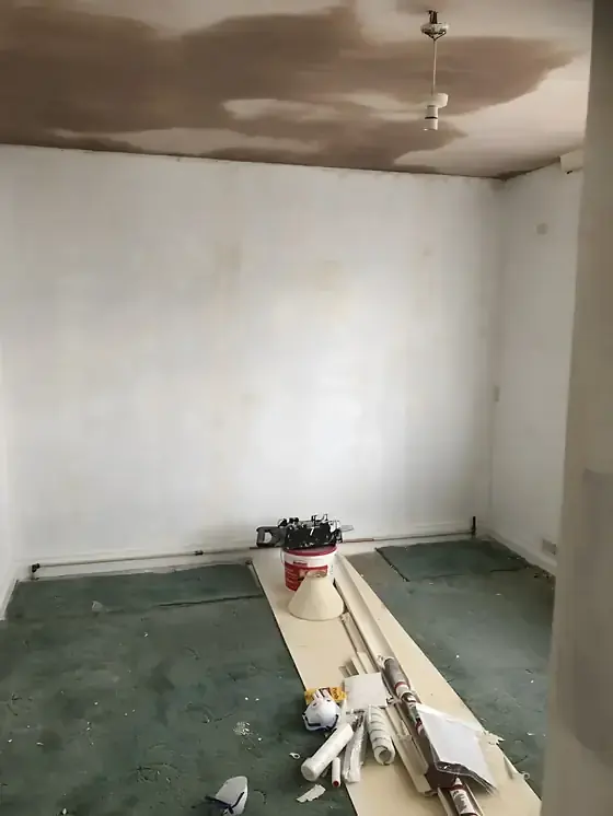 Newly plastered room with plaster curing, bare patches on the ceiling and tools on the carpet