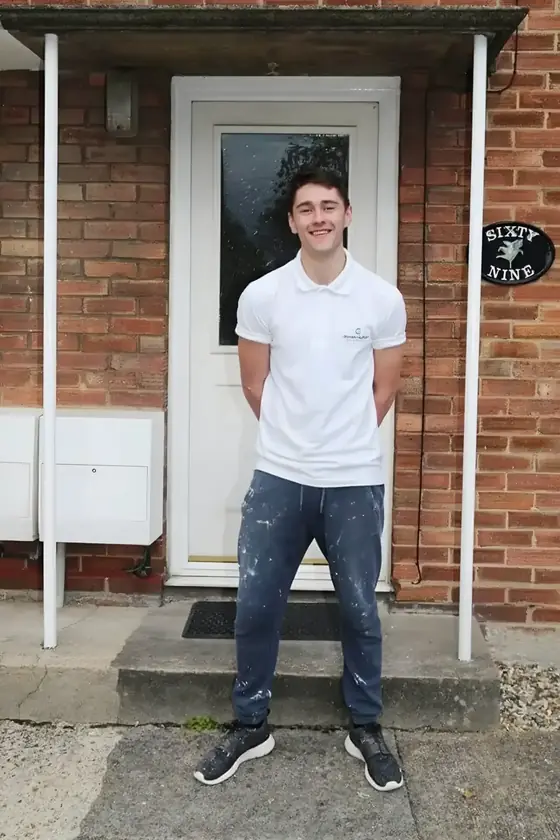 Young decorator in white polo shirt and paint-spotted jeans outside a white front door