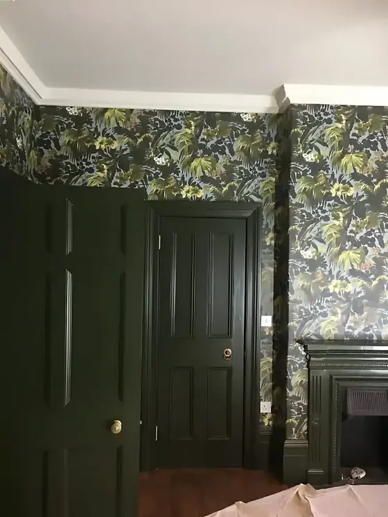 Dark green panelled doors and tropical leaf wallpaper around a fireplace, with white ceiling coving