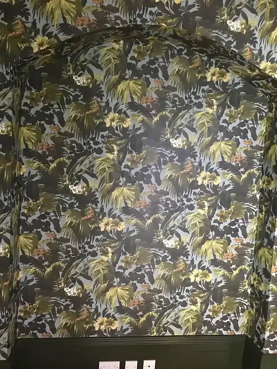 Deep green painted skirting board below tropical leaf wallpaper in green and gold