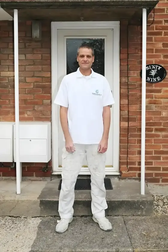 Decorator in white painter's overalls standing at a red brick house with a white front door