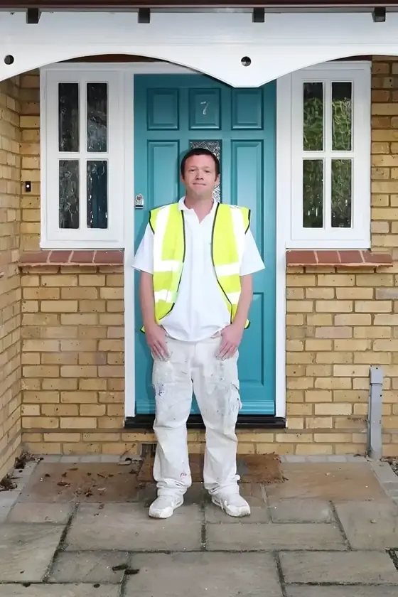 Decorator in hi-vis vest and white overalls standing before a turquoise front door
