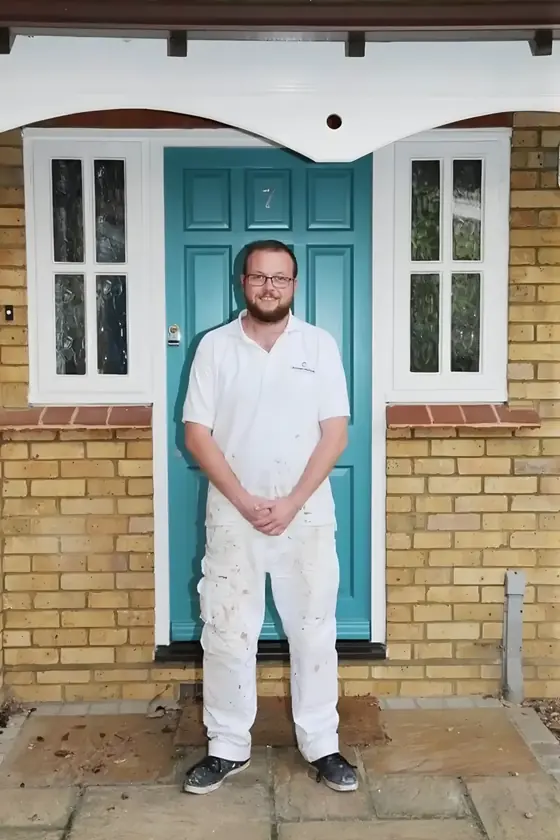 Bearded decorator in white overalls standing in front of a freshly painted turquoise front door
