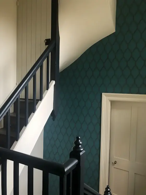 Stairwell with dark teal geometric wallpaper, black balustrade and white painted panelling