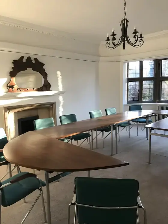 Meeting room with white cornice, long wooden table, green chairs and a painted fireplace