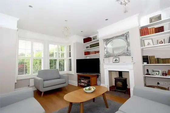Living room with white woodwork, built-in shelves, stove fireplace, grey armchair and ornate mirror