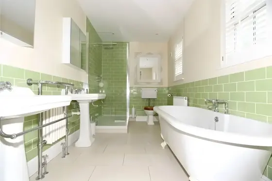 Bathroom with sage green metro tiles, freestanding bath, pedestal basins and cream painted walls
