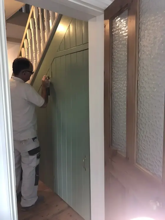 Decorator in a mask painting a sage green panelled door under the stairs