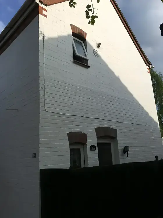 Tall white painted brick gable wall with a small window and red-brick arch details
