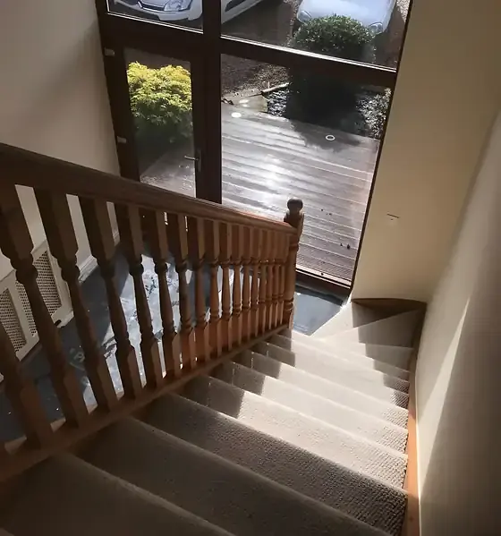 Staircase with varnished pine balusters, handrail and newel post above carpeted steps leading down to a glazed door