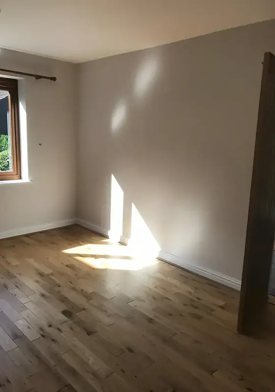 Empty room with freshly painted neutral walls and a sunlit oak floor beside a window