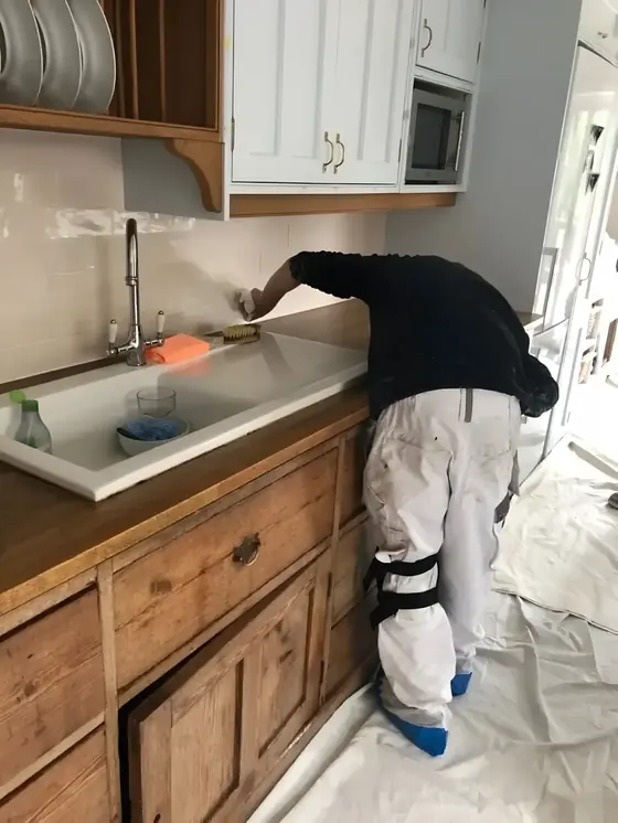 Decorator in white overalls and knee pads preparing kitchen units, with dust sheets on the floor
