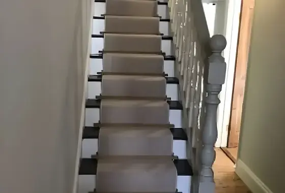 Carpet-runner staircase with black painted risers, white painted spindles and a grey newel post