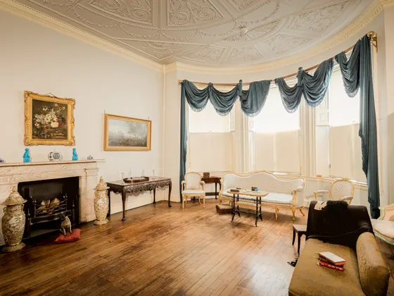 Period drawing room with cream walls, an ornate plaster ceiling, marble fireplace and bay window