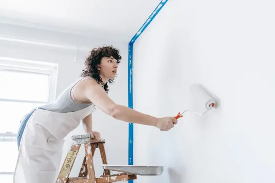 Decorator rolling white paint onto a freshly masked wall