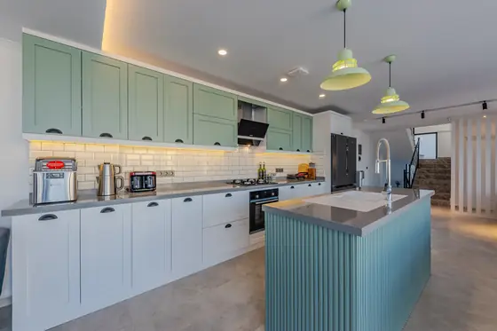 Kitchen with sage green painted cabinets, white metro tiles and a fluted teal island