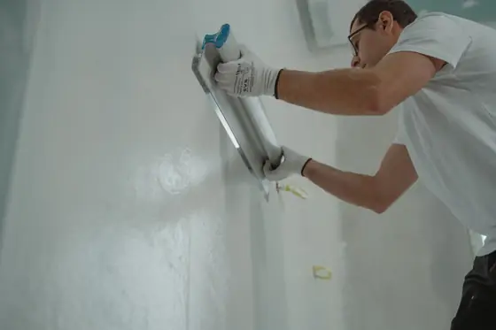 Plasterer skimming a wall smooth with a wide trowel