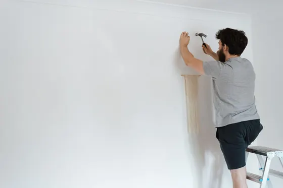 A man working at a plain white wall from a step ladder