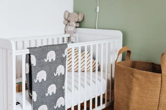 A white cot against a sage green nursery wall