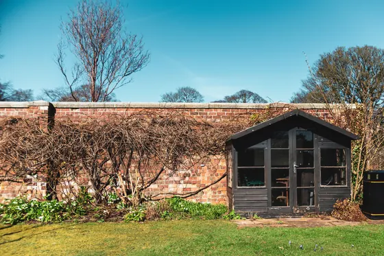 A dark painted summerhouse with glazed doors against an old brick wall