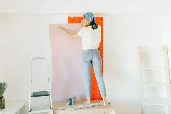 Strip of patterned wallpaper being hung on a bedroom wall beside a stepladder