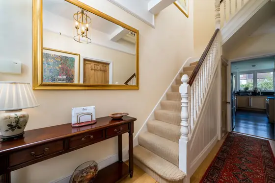 English hallway with a white painted banister, carpeted stairs and antique console table